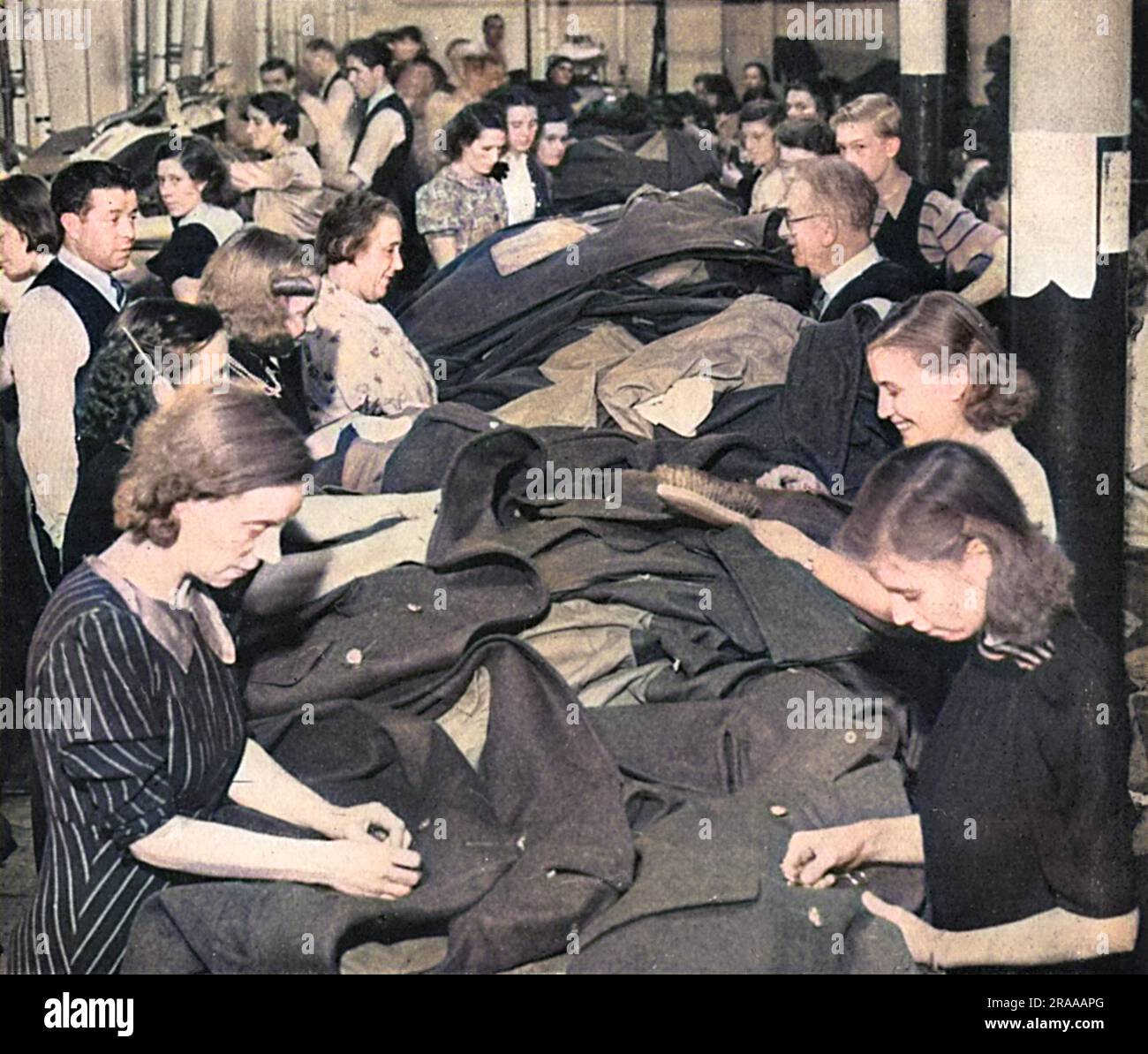 A great effort being made to get a big supply of greatcoats finished quickly so that no men may be caught by winter's grip without them.  Workers in an army clothing factory busy sewing buttons on coats for British servicemen during World War Two.     Date: 1939 Stock Photo