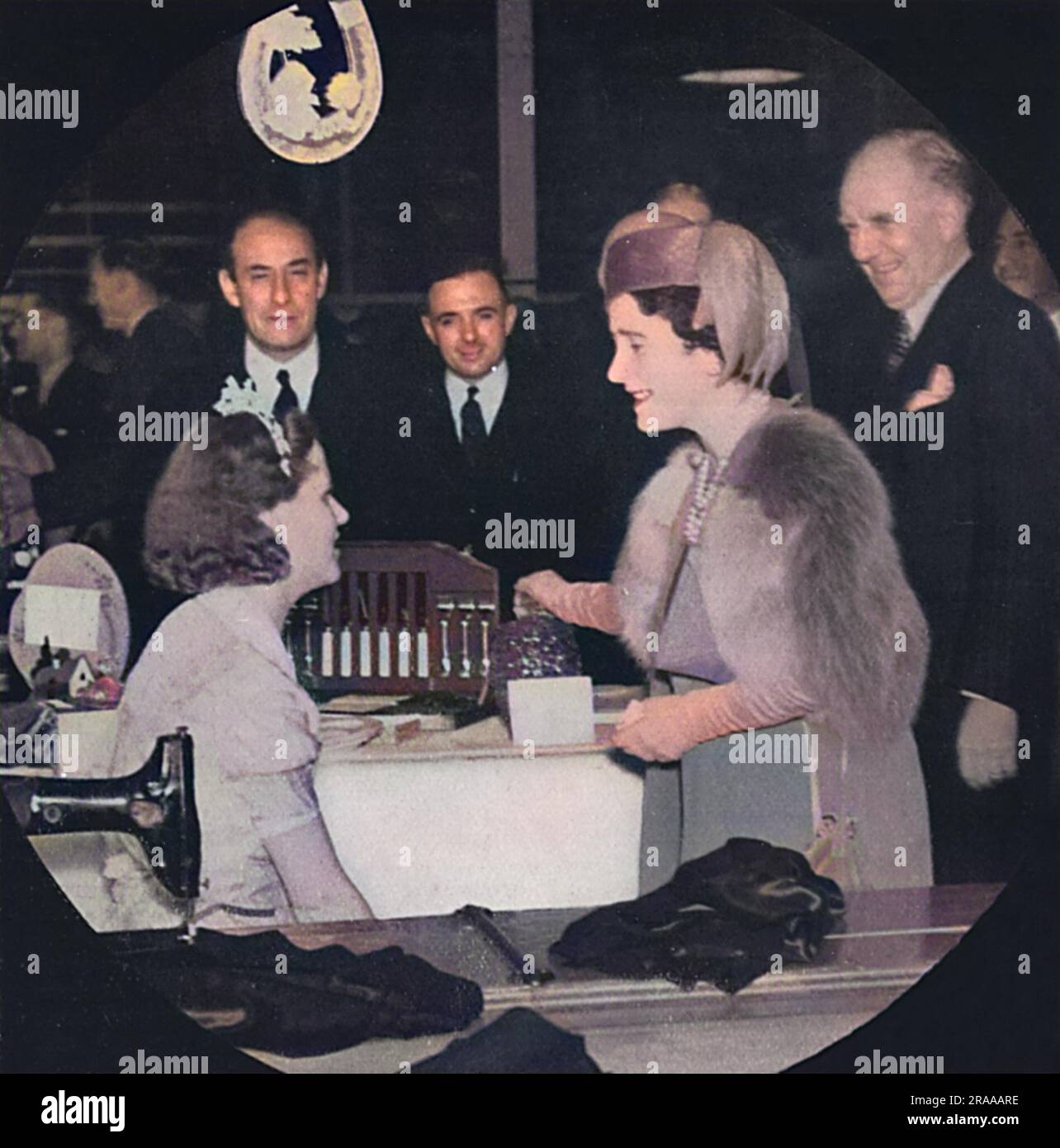 While touring a busy army clothing factory, Queen Elizabeth meets Miss Edith Nichols, a bride-to-be who talked to the Queen while wearing her wedding dress with orange blossom in her hair.     Date: 1939 Stock Photo