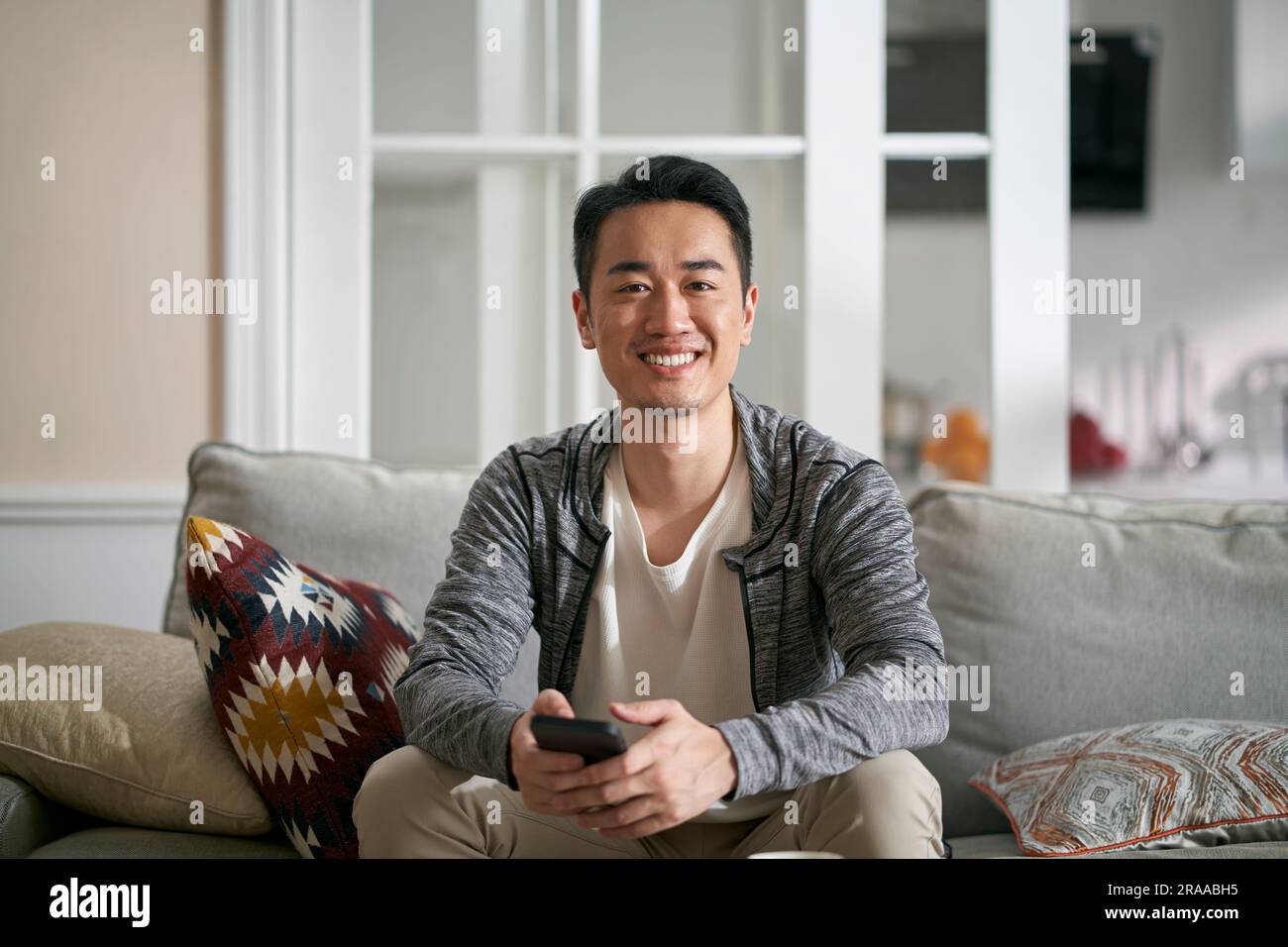 home portrait of a young happy asian man sitting on family couch looking at camera smiling Stock Photo