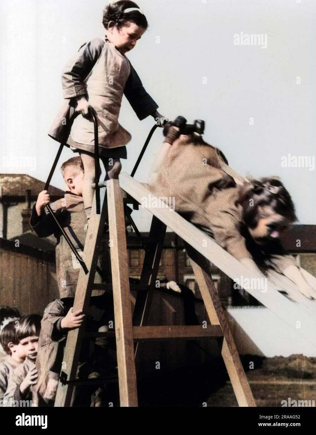 Nursery school children playing on slide in playground and waiting patiently in a queue to ascend slide     Date: 1930s Stock Photo