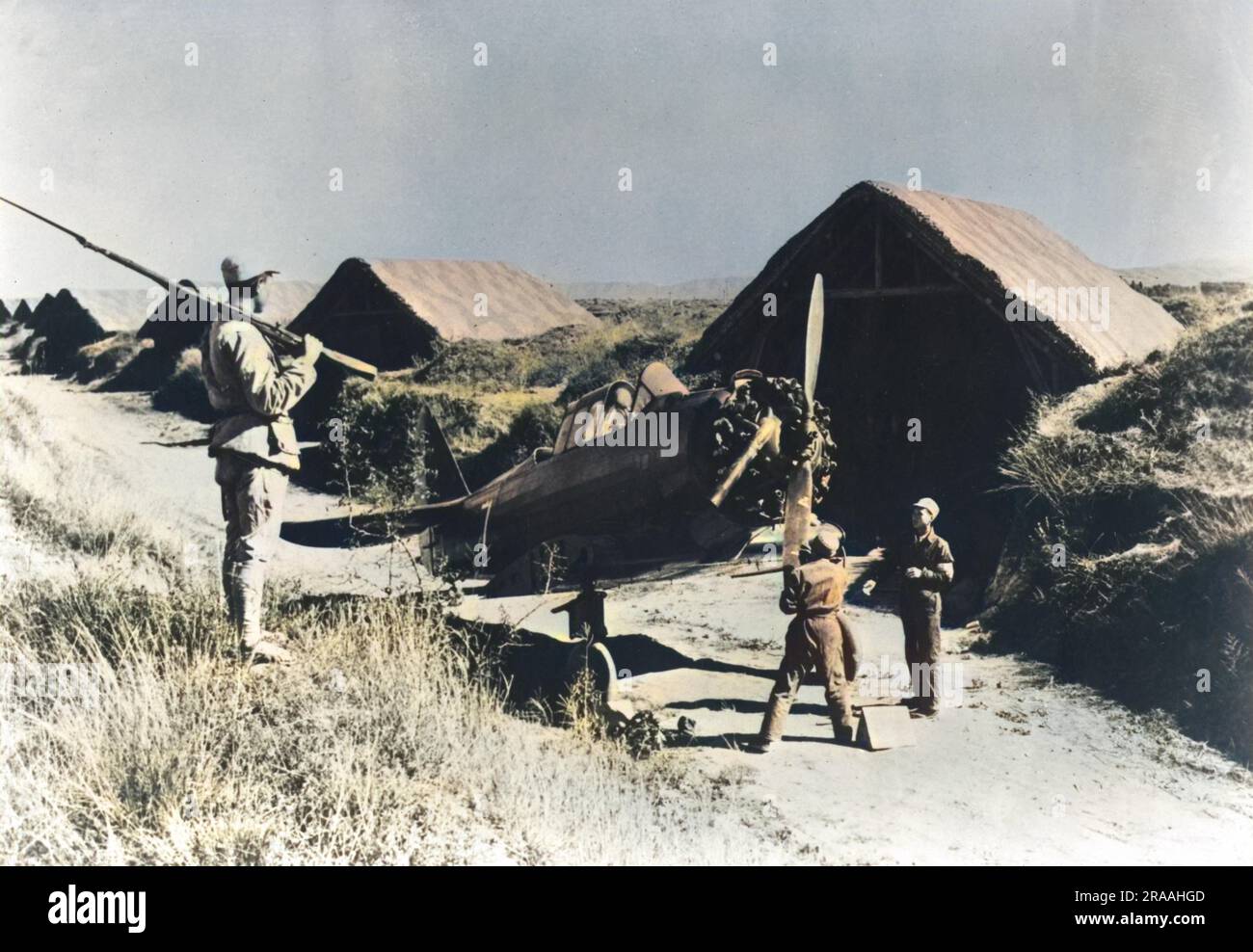 With a Chinese soldier standing guard, repair work on a U.S. fighter plane is carried out somewhere in China. The camouflaged huts in the background act as cover for the American planes     Date: 1943 Stock Photo