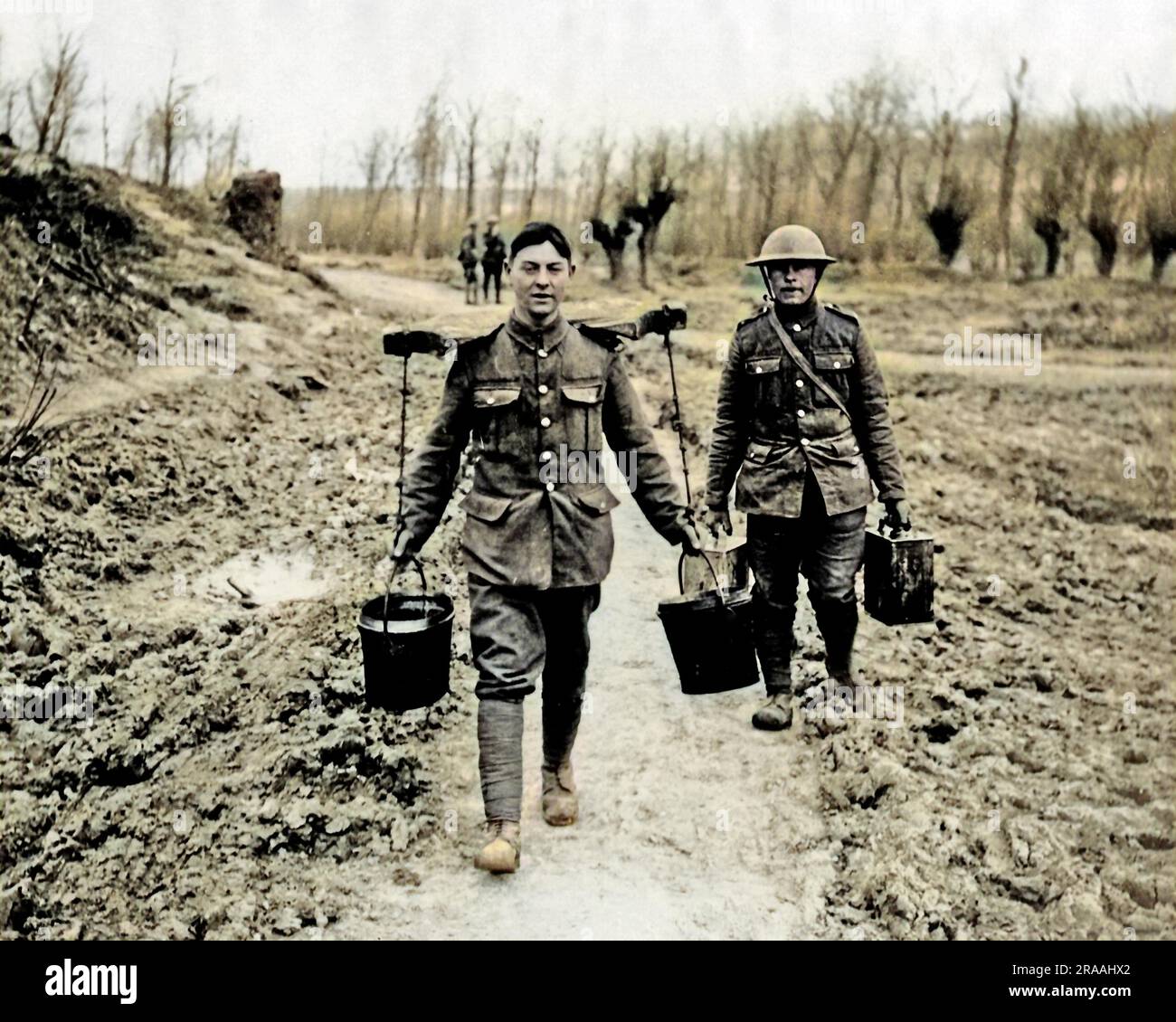 A British soldier using a yoke to carry two buckets of water on the Western Front during World War One.  The man behind him is carrying two cans.     Date: circa 1916 Stock Photo