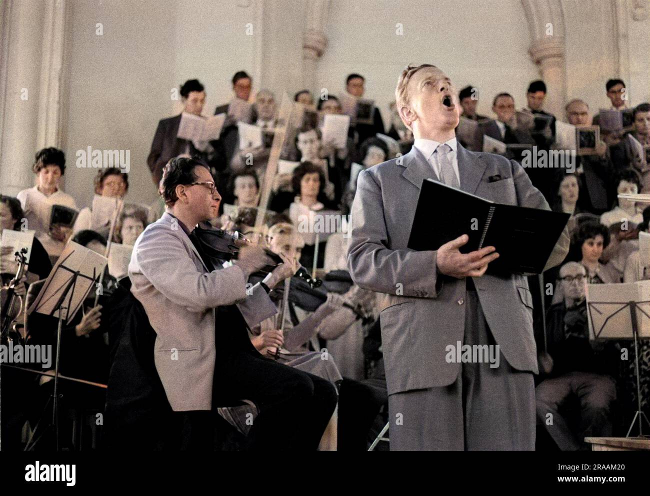 Peter Pears rehearsing the title role in Britten's Saint Nicolas at Orford Church, 23 June 1963.  The Aldeburgh Festival Choir and the choir pf Ipswich High School for Girls fills the background, with Emanuel Hurwitz, left, leading the English Chamber Orchestra     Date: 1963 Stock Photo