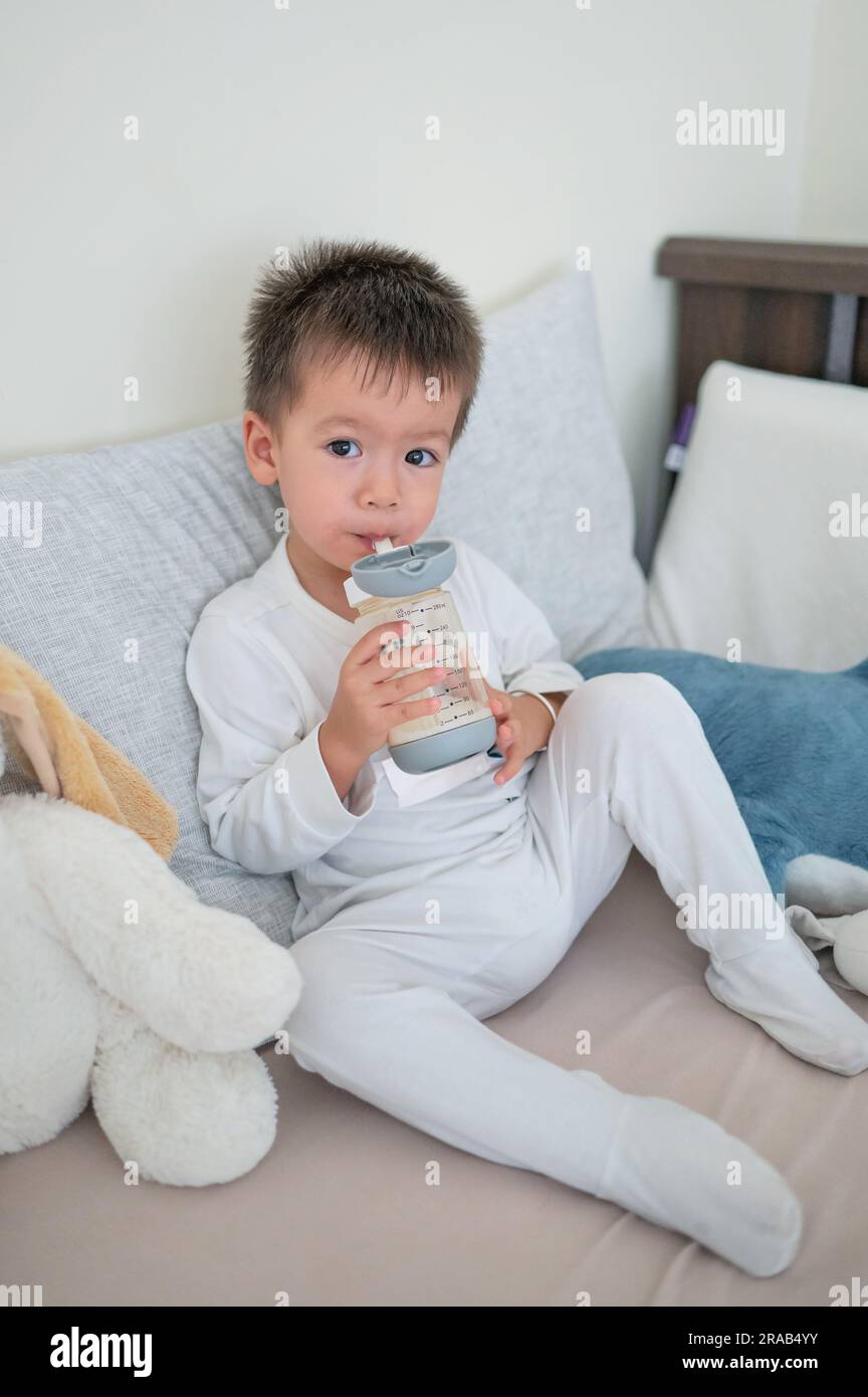 2 years old baby boy sits on the bed, happily drinking milk from a