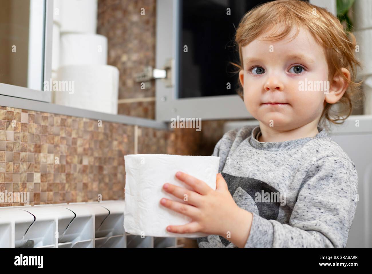 A cute boy is holding toilet paper roll in bathroom. Young boy with