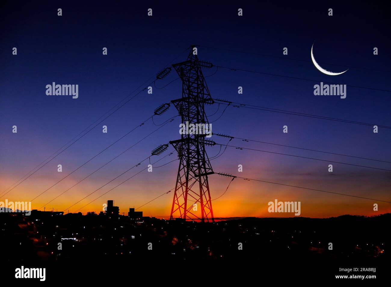 Electricity transmission tower silhouetted against blue sky at dusk Stock Photo