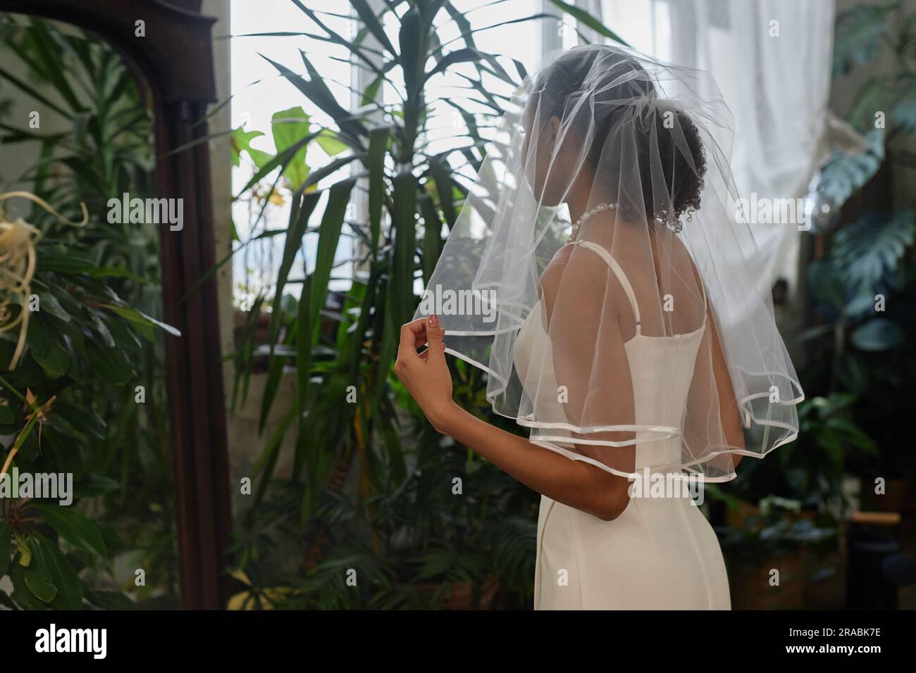 Portrait of black young woman as young bride wearing wedding gown and looking in mirror Stock Photo