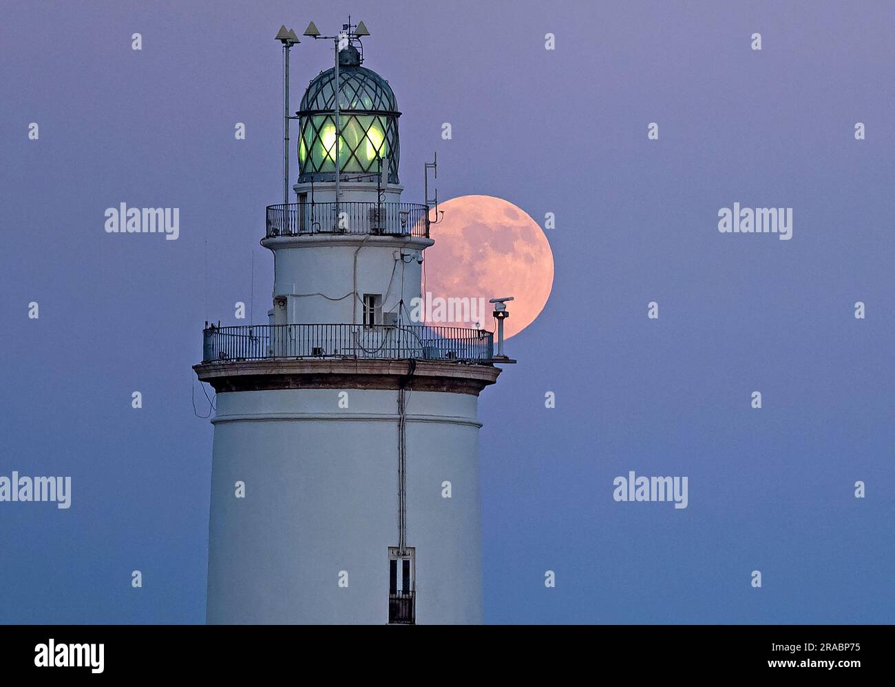 The buck moon rising in the sky over a lighthouse is seen at port of Malaga. At the beginning of July, the full deer moon takes place as one of the most striking astronomical events of the month. When the full moon takes place it appears larger and brighter than normal. Stock Photo