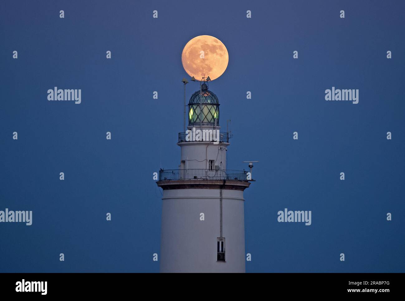 The buck moon rising in the sky over a lighthouse is seen at port of Malaga. At the beginning of July, the full deer moon takes place as one of the most striking astronomical events of the month. When the full moon takes place it appears larger and brighter than normal. Stock Photo