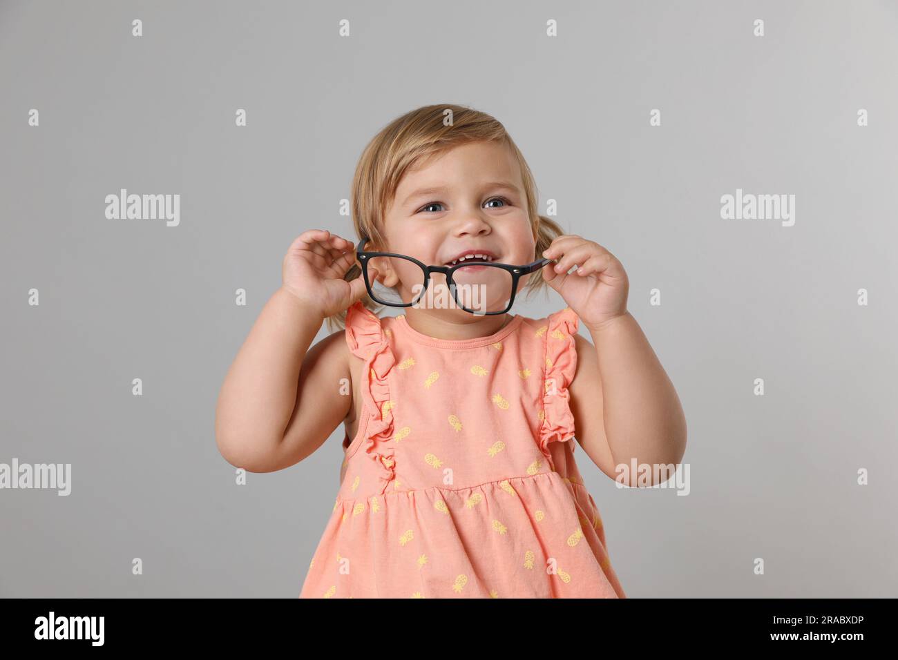 Cute little girl with glasses on light grey background Stock Photo Alamy