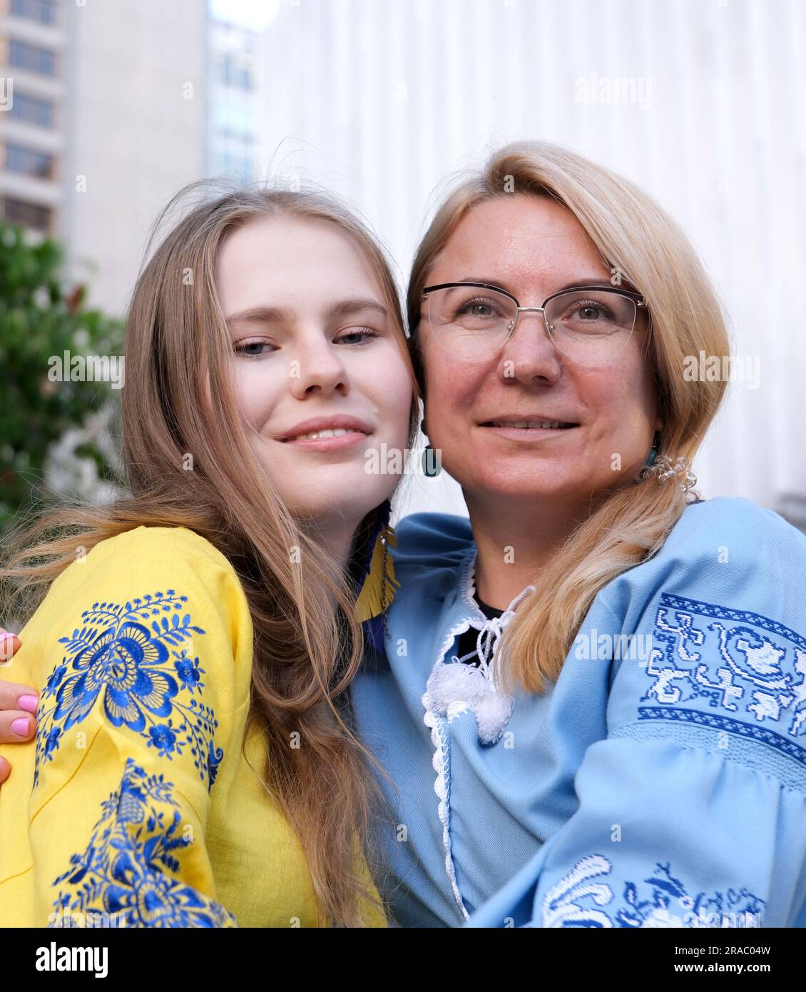 Happy senior woman enjoying in daughter's affection on Mother's day. mother and daughter in embroidered shirts blue and yellow blouse cute family relationship close-up portrait face outdoors Stock Photo