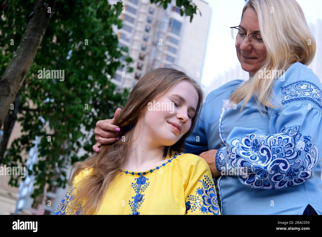 Happy senior woman enjoying in daughter's affection on Mother's day. mother and daughter in embroidered shirts blue and yellow blouse cute family relationship close-up portrait face outdoors Stock Photo