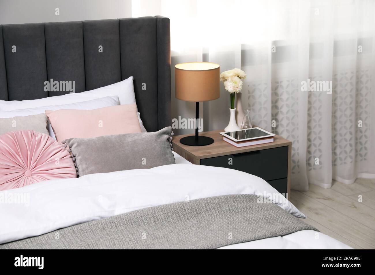 Comfortable bed with cushions, lamp and different decor on bedside table in room. Stylish interior Stock Photo