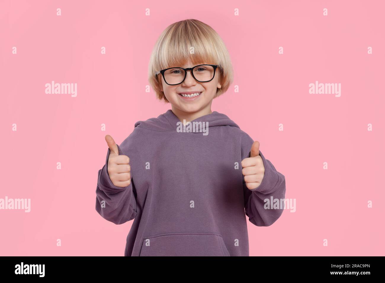 Cute little boy in glasses showing thumbs up on pink background Stock
