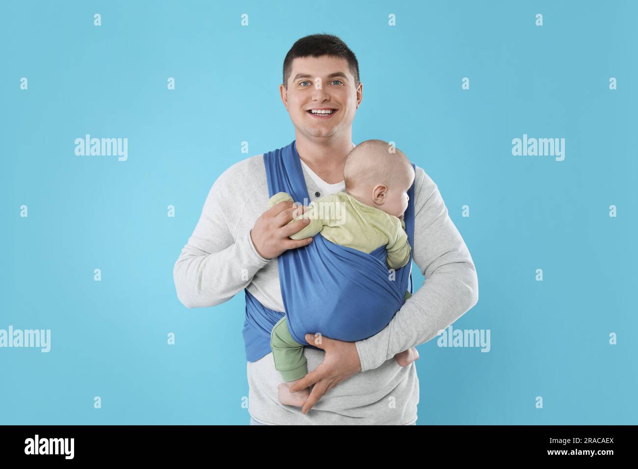Father holding his child in sling (baby carrier) on light blue background Stock Photo Alamy