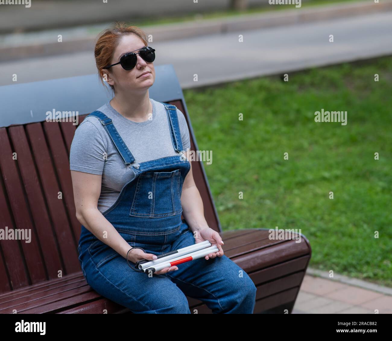 Blind pregnant woman holding folding cane while sitting on bench Stock