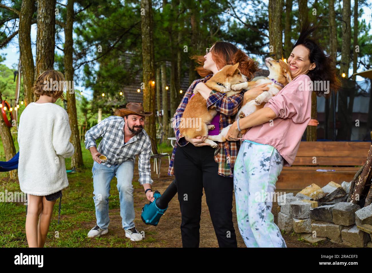 Funny family moment with father using garden blower for teasing his wife and daughter holding dogs Stock Photo