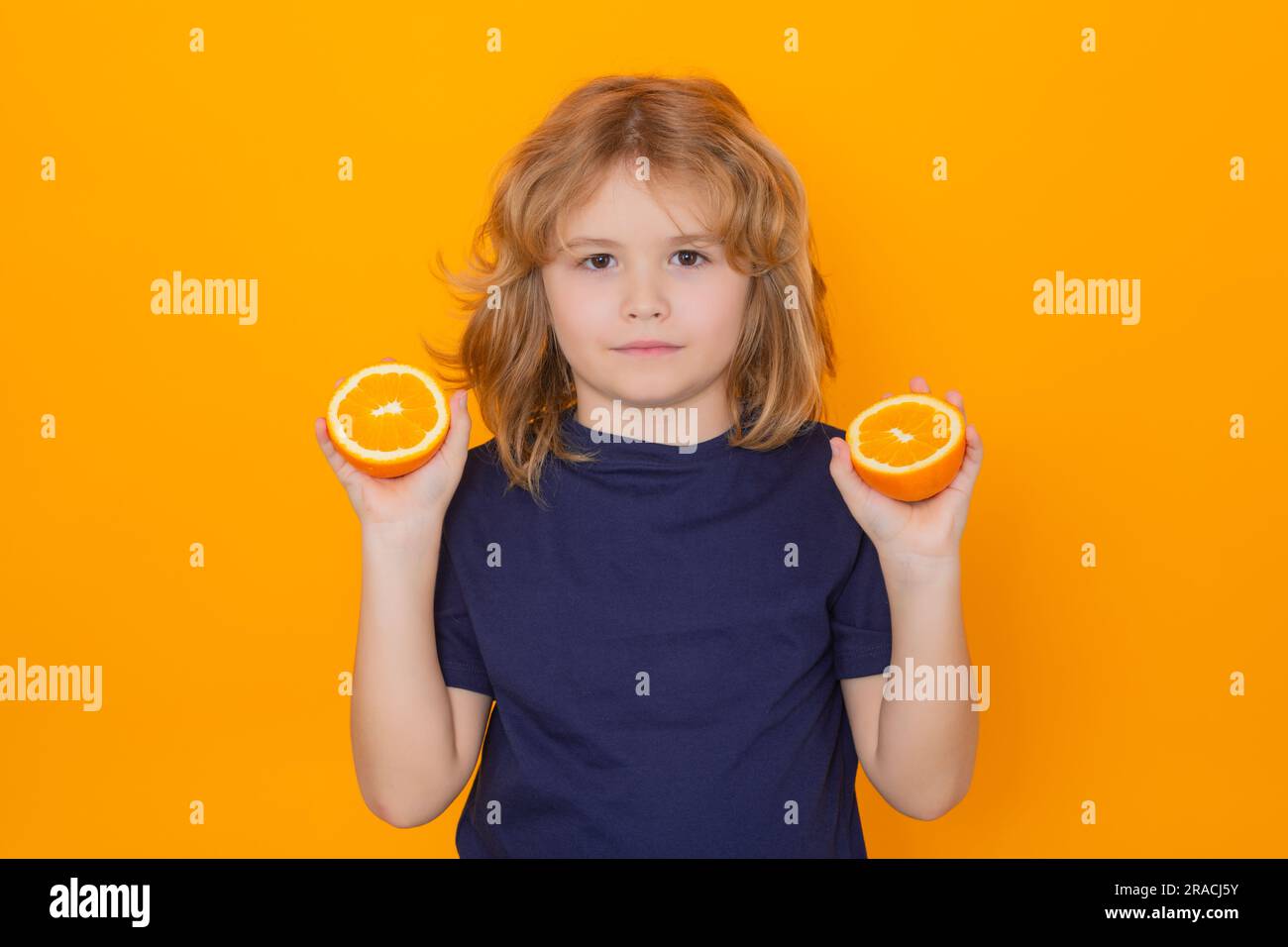 Kid with orange in studio. Studio portrait of cute child hold orange isolated on yellow background Stock Photo