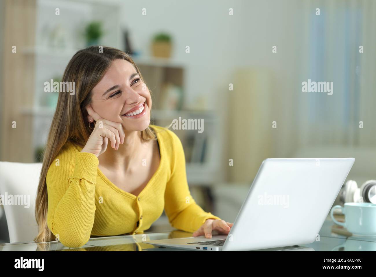 Happy woman at home dreaming looking above with a laptop Stock Photo