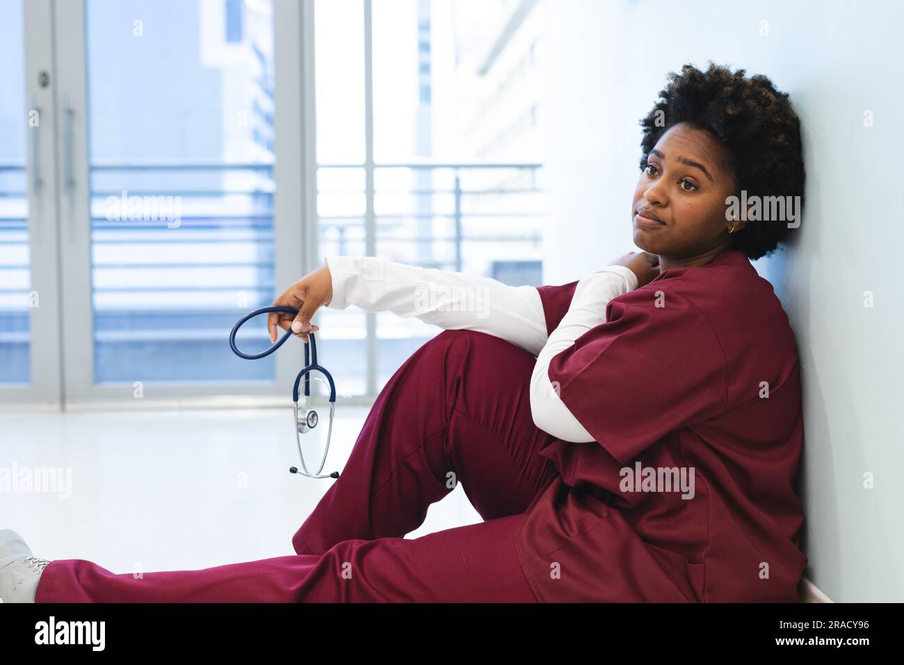Tired african american female doctor wearing scrubs, sitting on floor