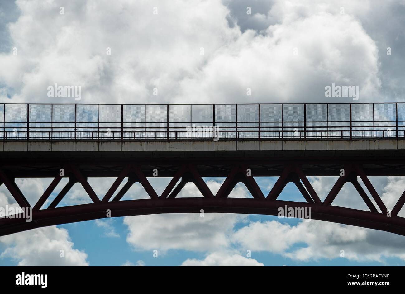 Image composed of a bridge in the foreground in backlight and castellated clouds contrasting with the blue sky in the background. Stock Photo