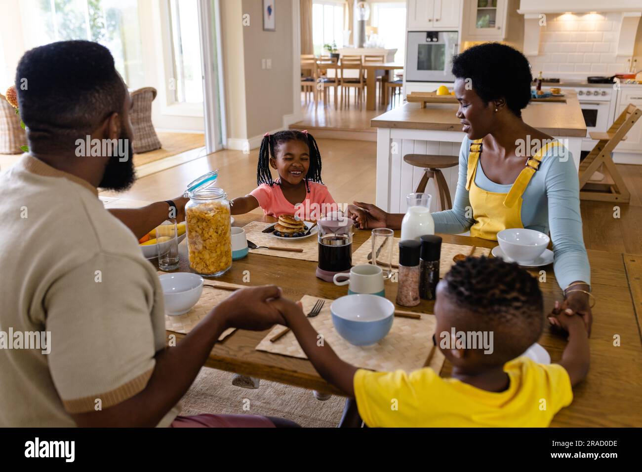 African american parents, children holding hands and saying grace at dining table before breakfast Stock Photo