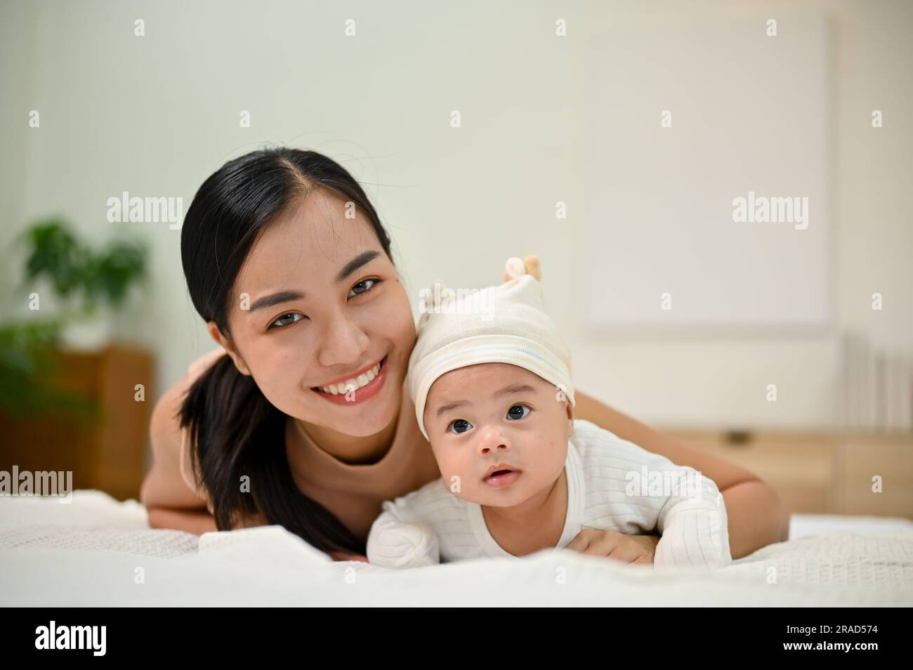 Sweet family moment. Young Asian mom lay down with her baby, smiling to camera. showing affection to her baby. Stock Photo