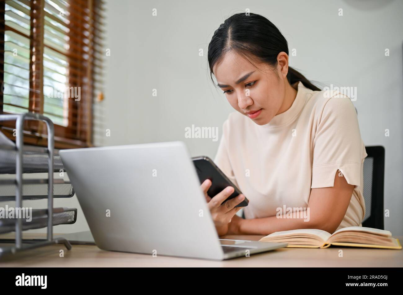Young stressful woman working from home with smartphone and laptop computer. Stock Photo
