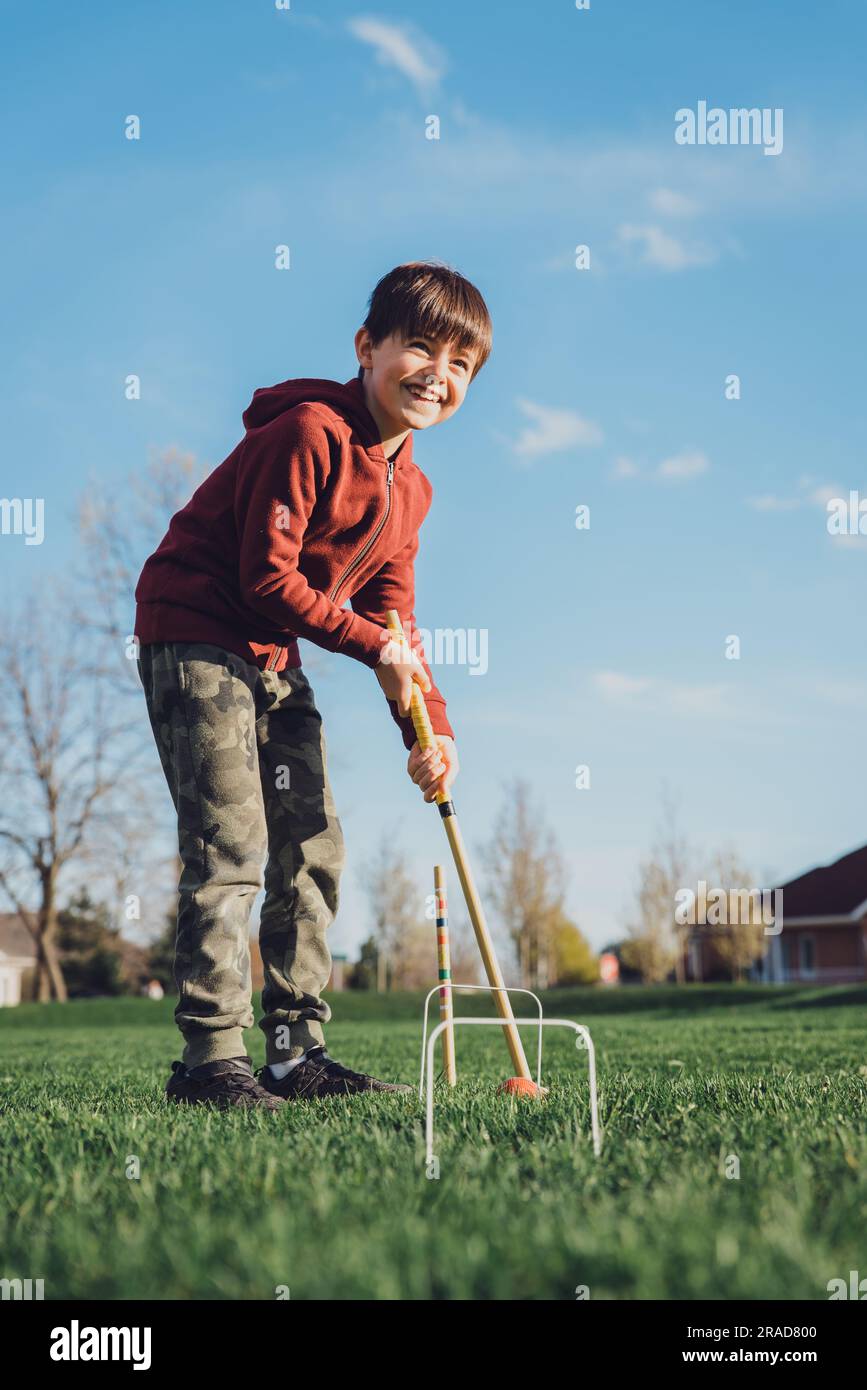 Young boy smiling as he is about to hit croquet ball with the mallet