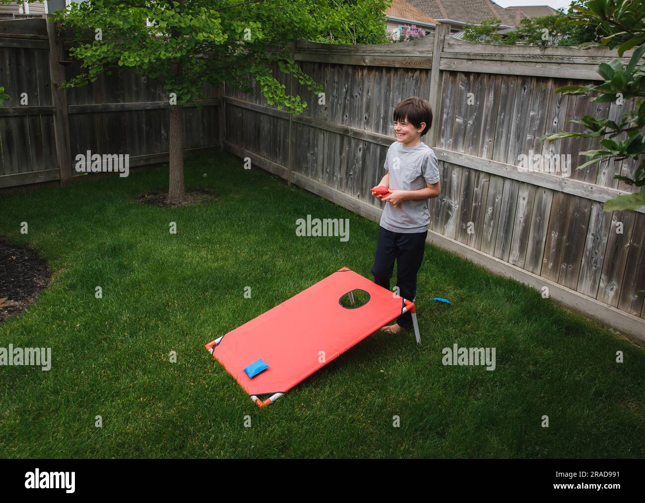 Happy young boy playing a corn hole game in a fenced backyard Stock