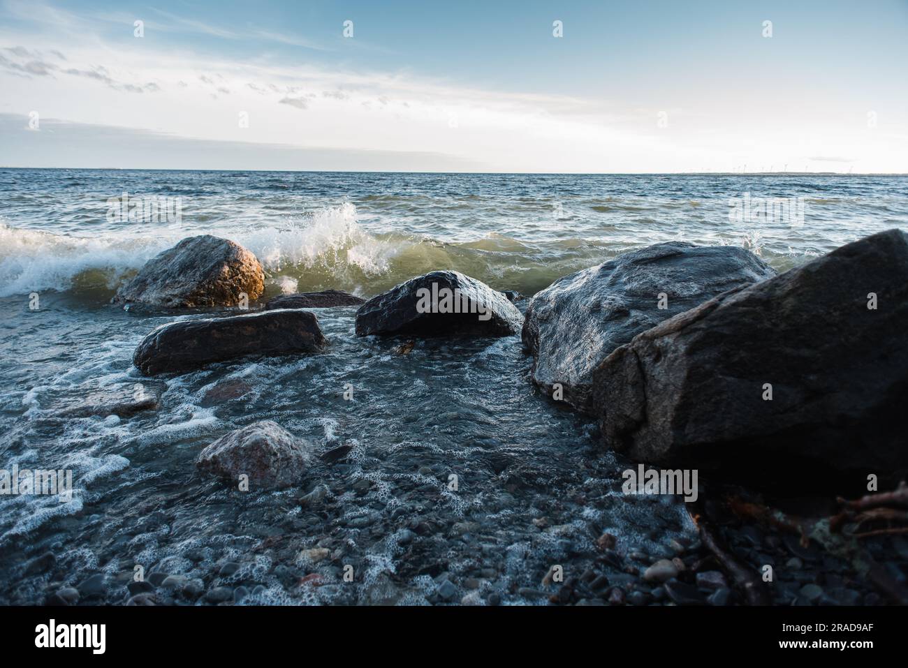Waves crashing against large rocks on shore of a lake during the day. Stock Photo