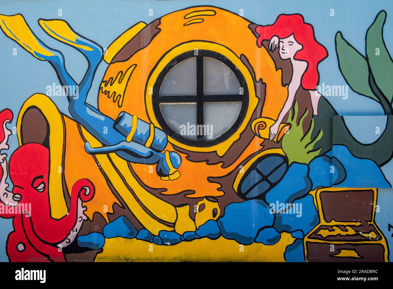 colourful cartoon graffiti wall or street art of a deep sea diver wearing a large diving helmet with scuba divers and mermaids. Stock Photo