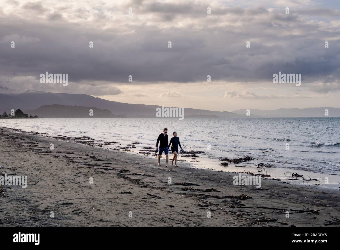 Young romantic couple walking Pōhara Beach water's edge, Takaka Coastal Region of Golden Bay, Abel Tasman National Park on South Island, New Zealand. Stock Photo