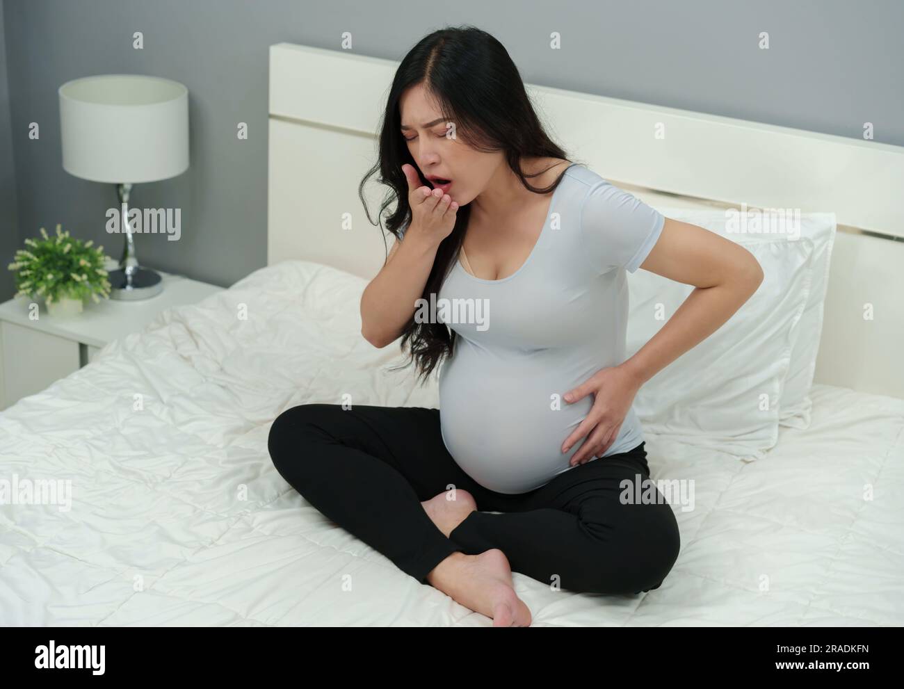 sick pregnant woman feeling unwell and coughing on a bed Stock Photo