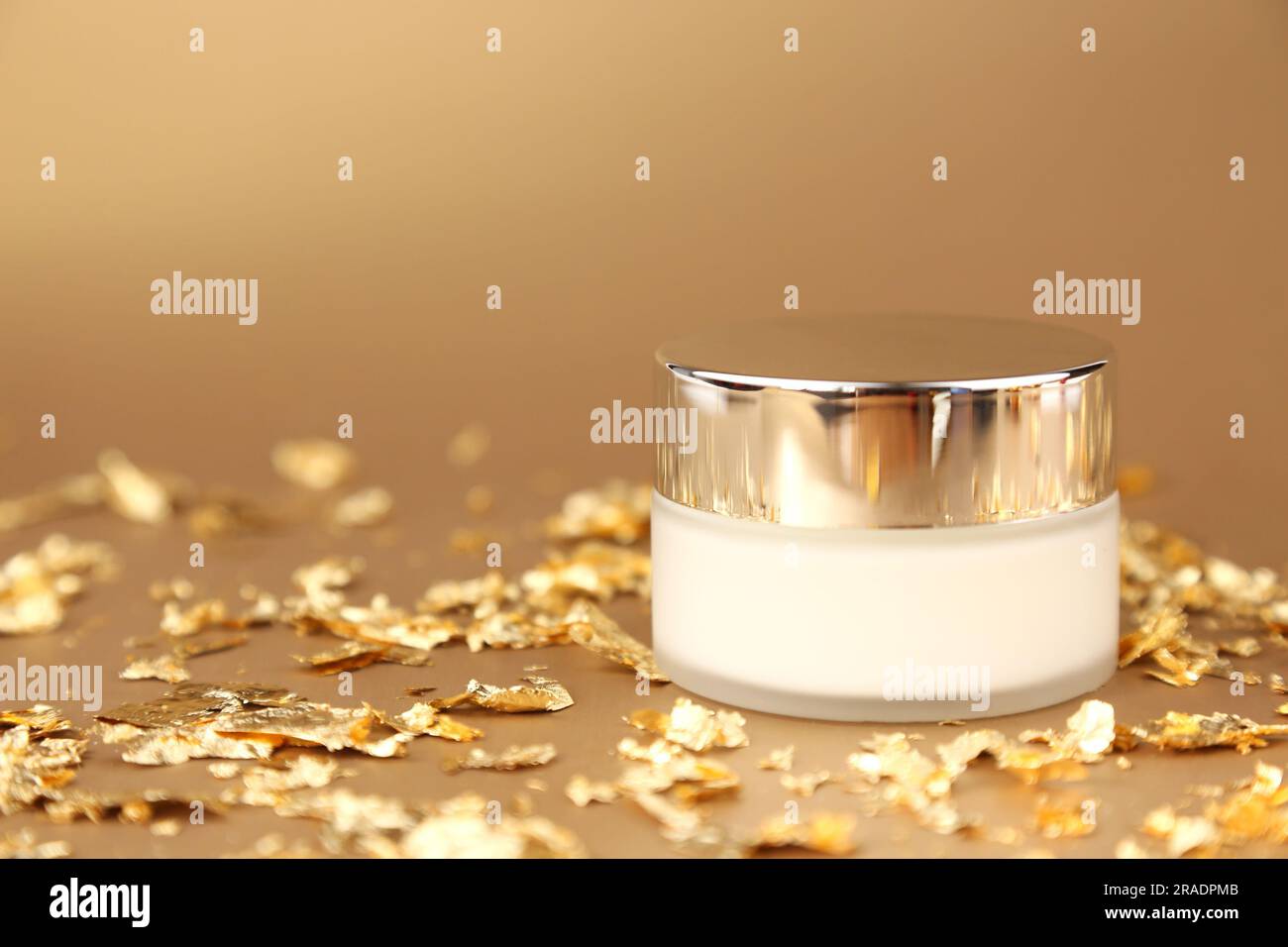 Cosmetic glass jar with white moisturizer. Luxurious antiaging day cream with isoflavones and active microparticles of gold and pieces of gold paper o Stock Photo