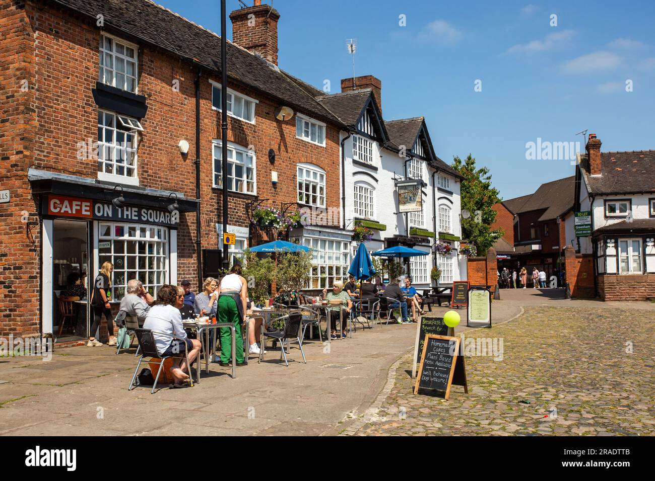 People sitting eating and drinking outside outdoors in the cobbled market square of the Cheshire market town of Sandbach Stock Photo