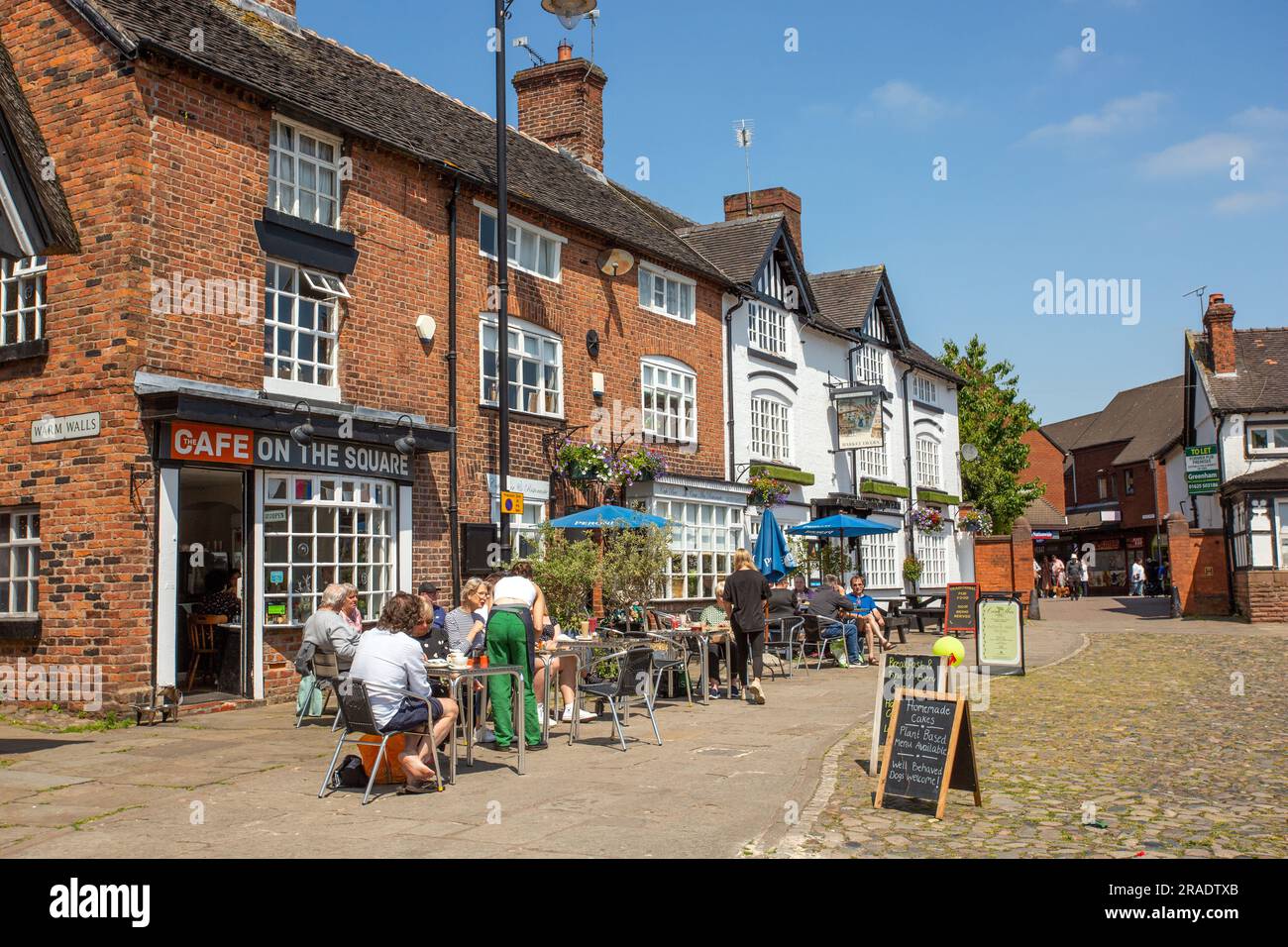 People sitting eating and drinking outside outdoors in the cobbled market square of the Cheshire market town of Sandbach Stock Photo