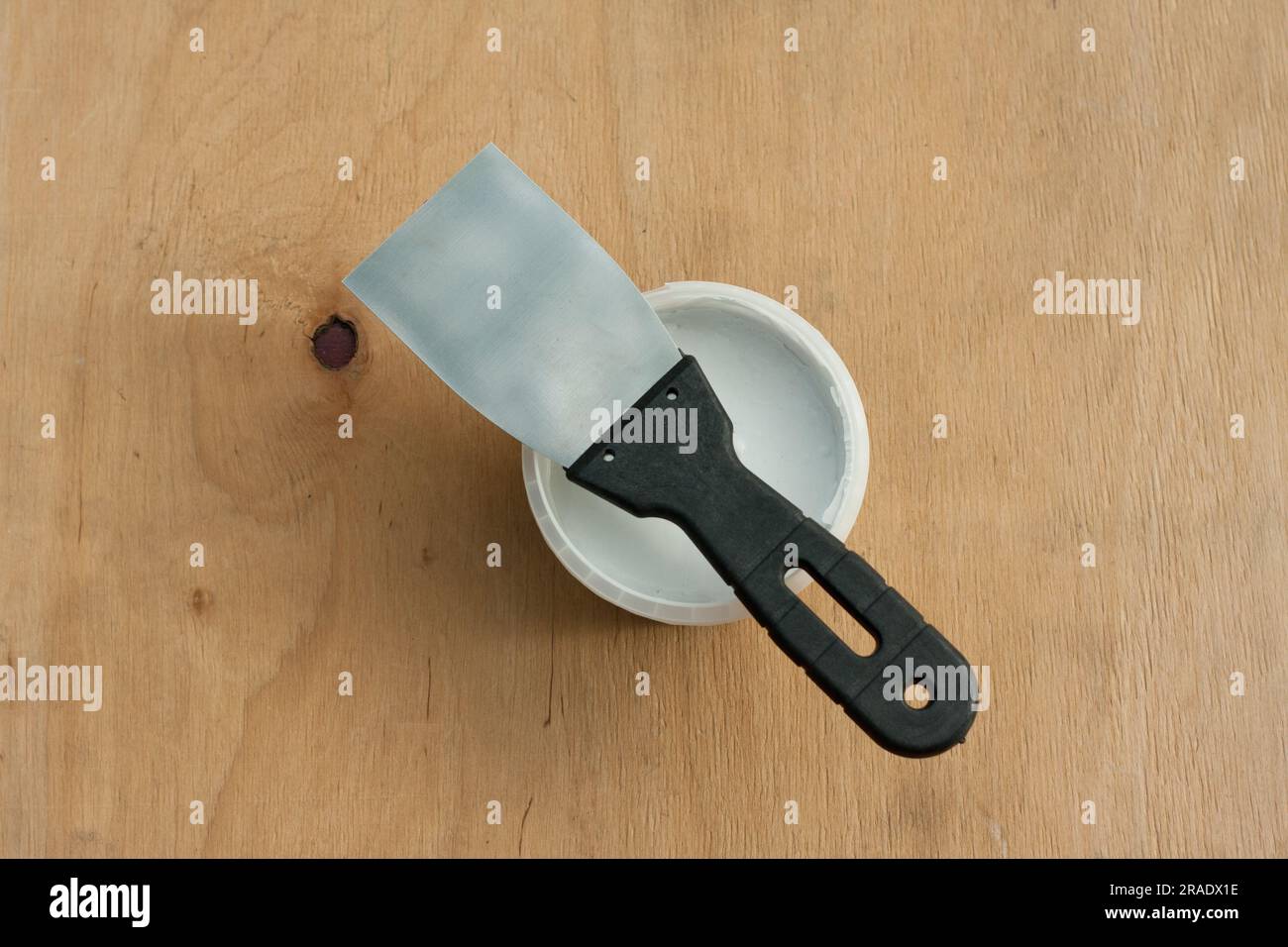 Construction putty knife and can of white putty on plywood surface