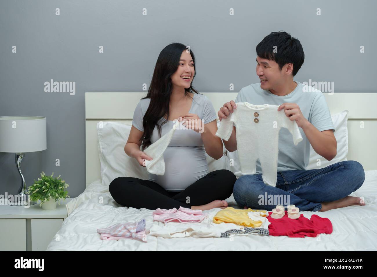 pregnant couple preparing baby clothes for newborn on a bed Stock Photo
