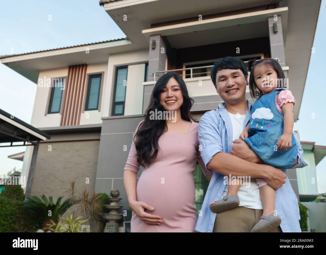 happy family standing outside their house, husband and pregnant wife ...