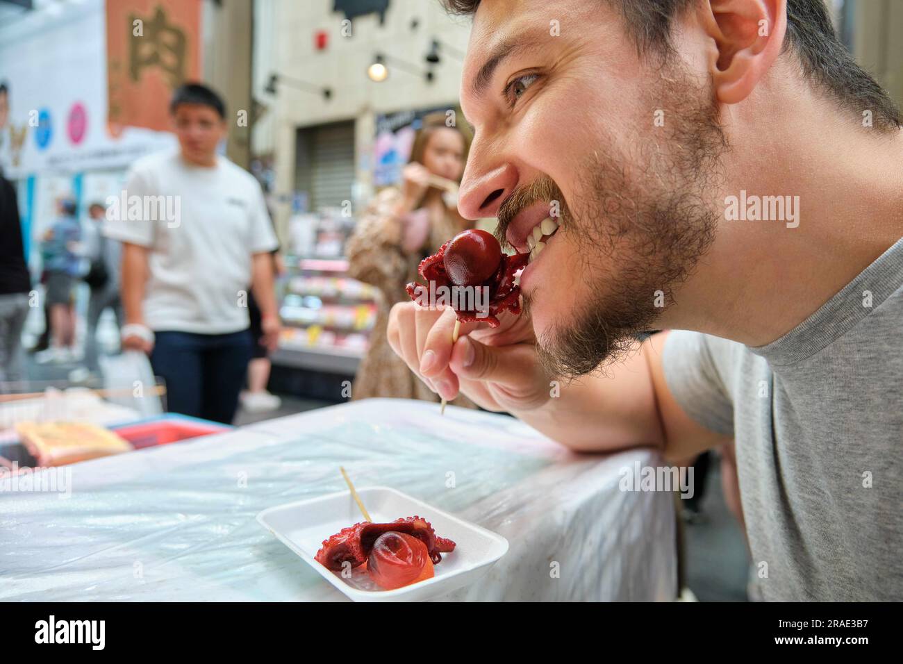 Tourist eating tako tamago, baby octopus, simmered and glazed in soy