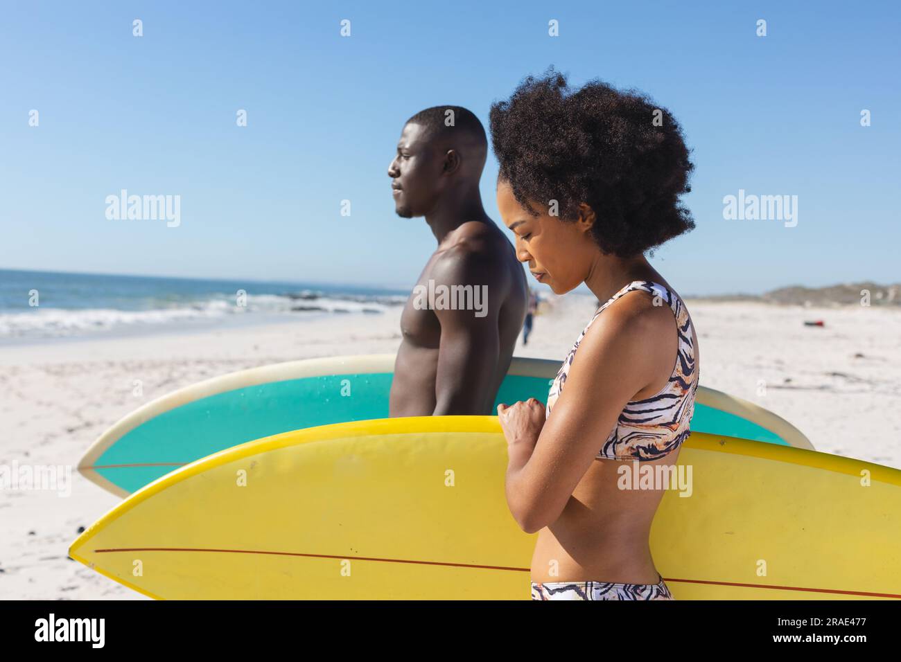 Fit african american couple holding surfboards standing on sunny beach by the sea Stock Photo