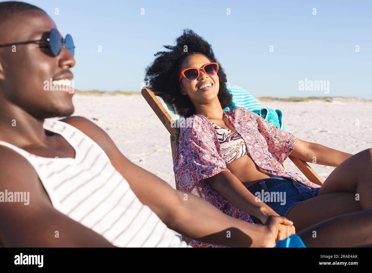 Happy african american couple sitting in deckchairs holding hands on ...