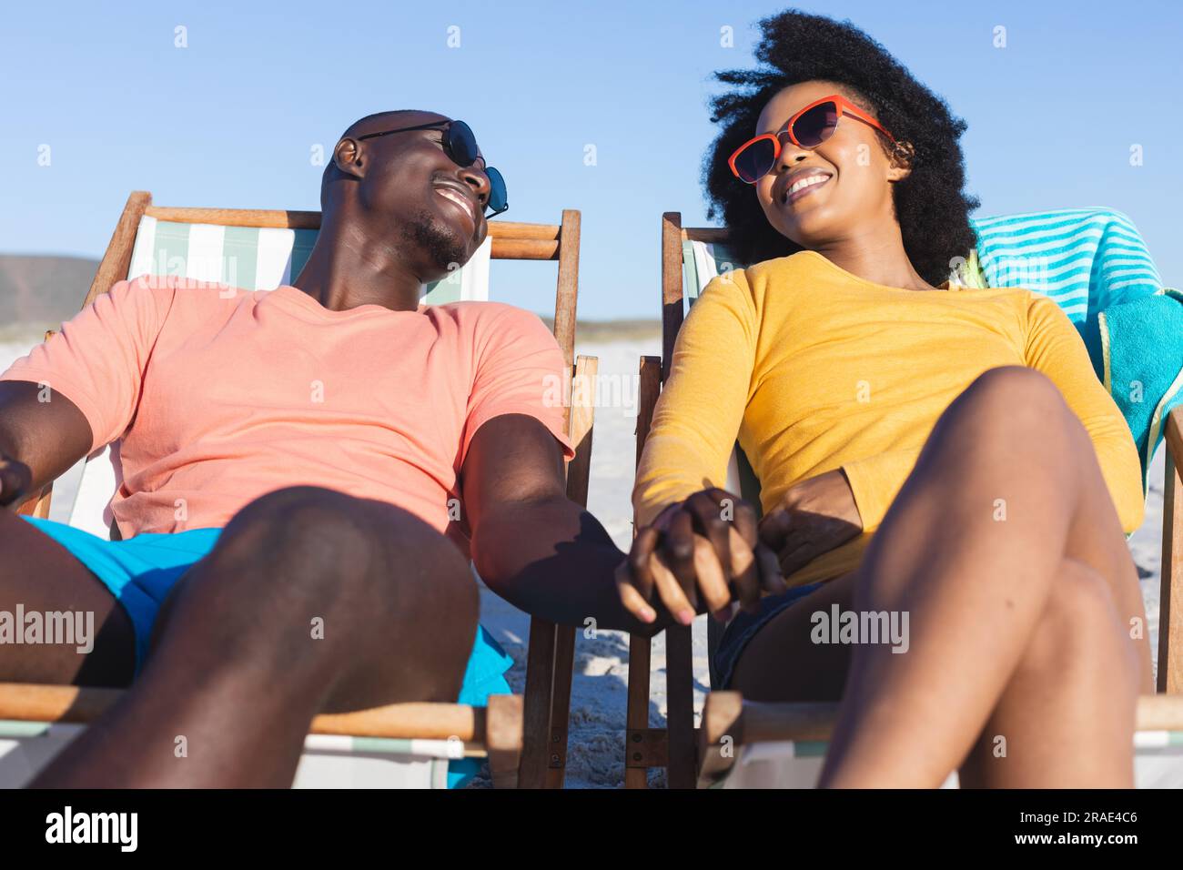 Happy african american couple sitting in deckchairs holding hands on ...