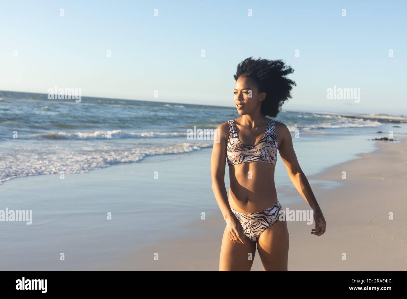 Happy african american woman in bikini walking on sunny beach by the