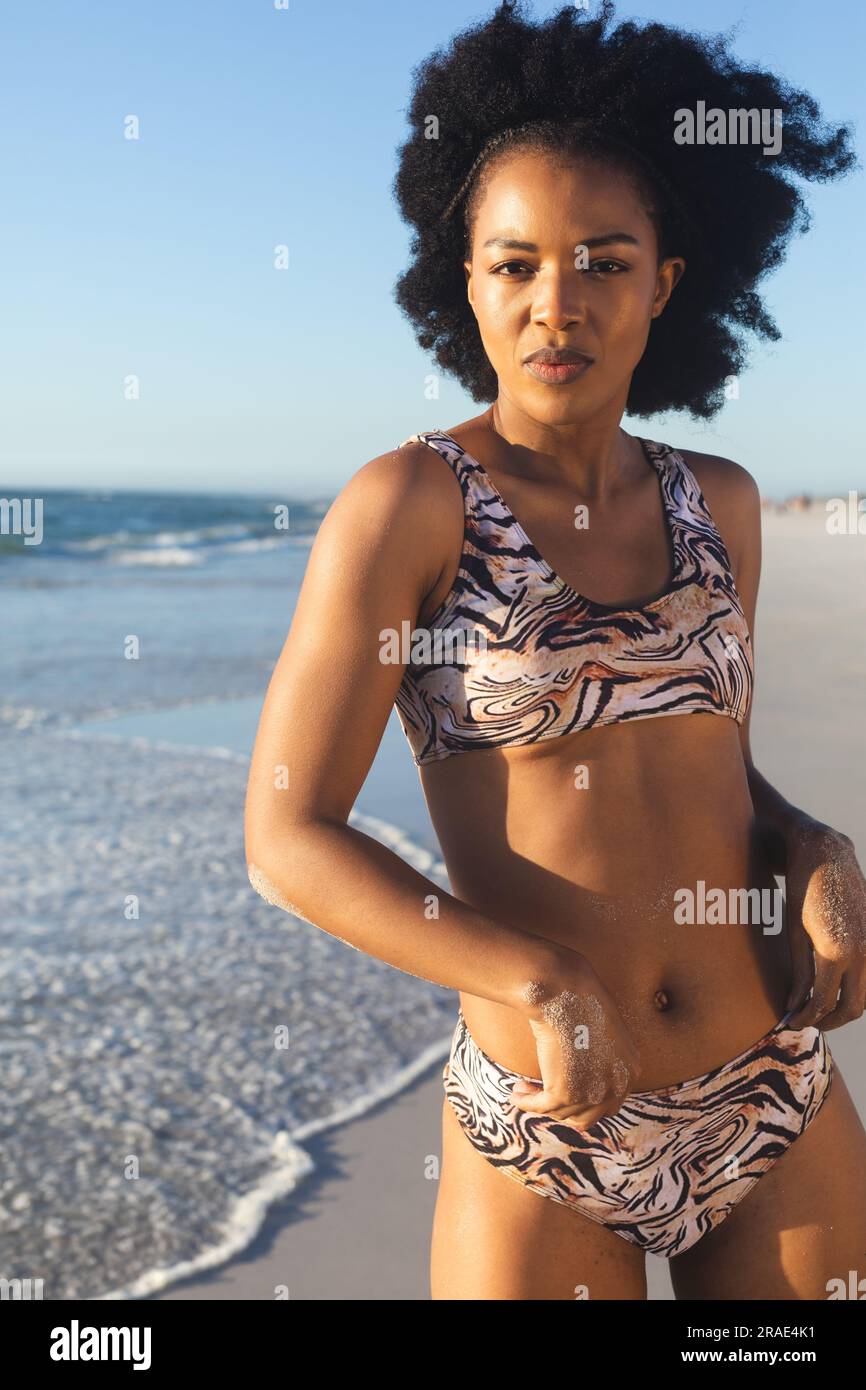 Portrait of african american woman in bikini standing on sunny beach by the sea Stock Photo