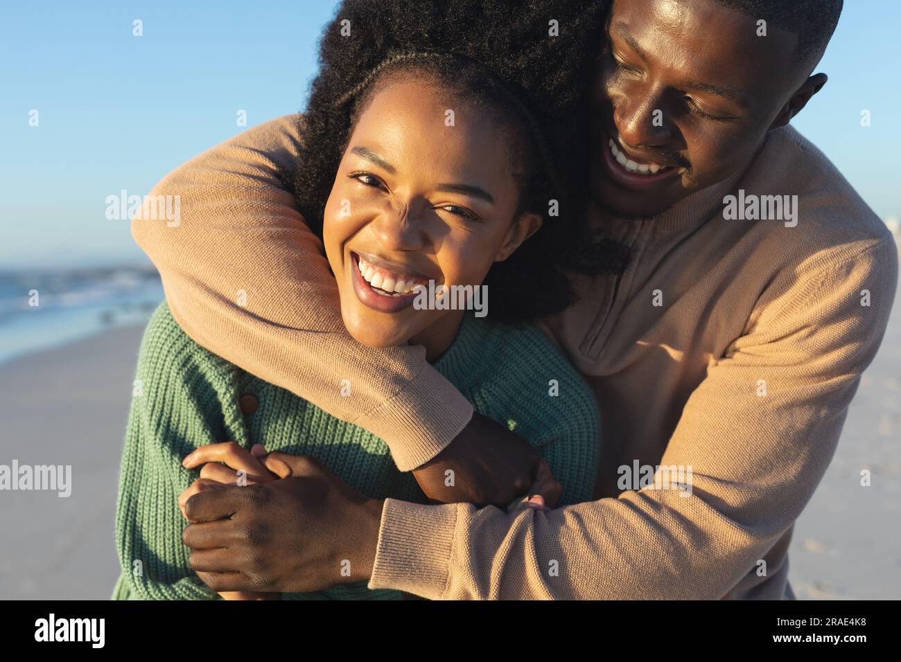 Portrait of happy african american couple embracing on sunny beach by ...