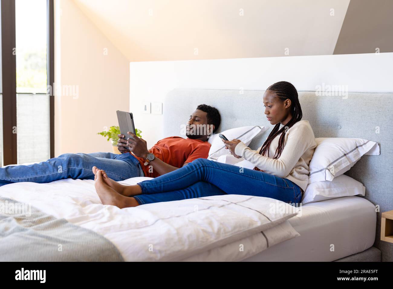 African american couple using tablet and smartphone lying on bed in ...