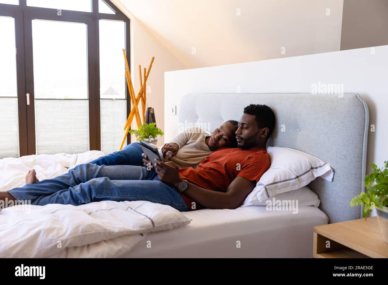 African american couple using tablet lying on bed in bedroom Stock ...
