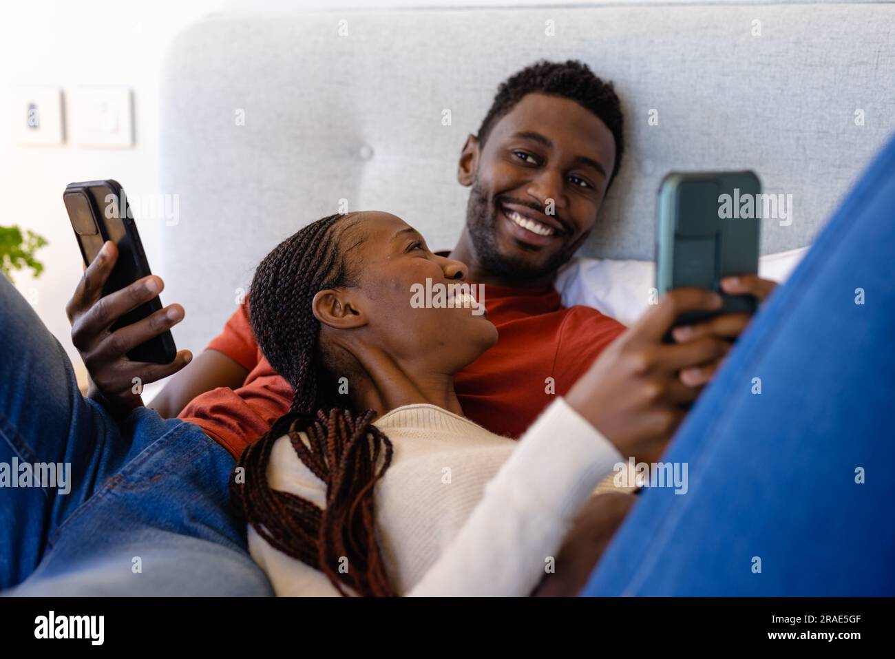 Happy african american couple using smartphones lying on bed in bedroom ...